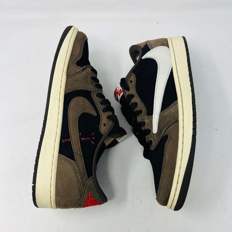 A brown and black Jordan 1 Retro Low OG SP Travis Scott Mocha with clean uppers and a large white swoosh sits on a Nike box. Two sets of extra laces in black and pink beside the box confirm their 100% authenticity. The shoe size is visible on the box label. Released in 2019.