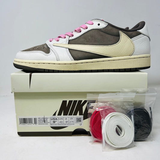 The Jordan 1 Retro Low OG SP Travis Scott Reverse Mocha is showcased on a Nike box, featuring a sleek white, brown, and beige upper with pink laces. Nearby are four additional lace sets: red, white, brown, and black, each in individual plastic bags.