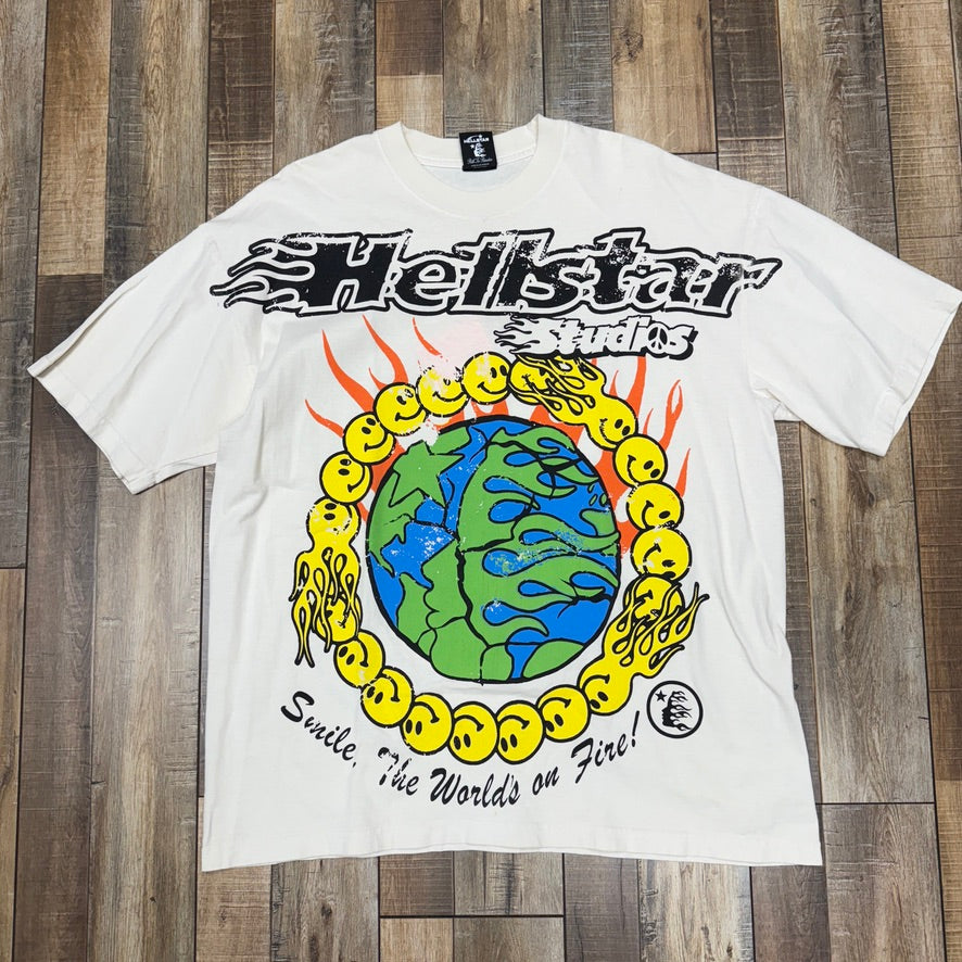 The pristine Hellstar Smile, The World on Fire T-shirt by HELL STAR features bold graphics: Hellstar Studios on top, a globe with yellow smiley faces and flames in the center, and Smile, the Worlds on Fire! at the bottom, all set against a white background.