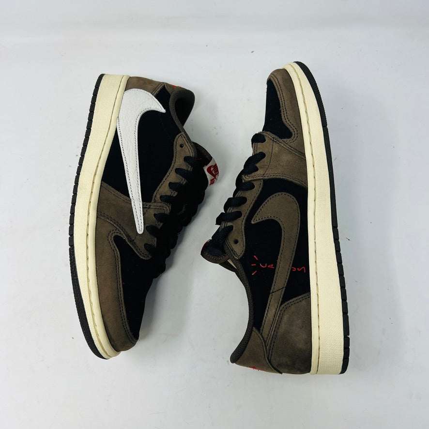 A brown and black Jordan 1 Retro Low OG SP Travis Scott Mocha with clean uppers and a large white swoosh sits on a Nike box. Two sets of extra laces in black and pink beside the box confirm their 100% authenticity. The shoe size is visible on the box label. Released in 2019.