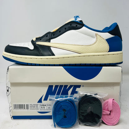 The Jordan 1 Retro Low OG SP Fragment x Travis Scott sneakers from Holy Ground Sneaker Shop feature blue, black, and cream colors with the iconic swoosh. Displayed on a Nike box, they include extra laces (blue, black, pink) in plastic packaging. These shoes exude clean style with minimal wear.