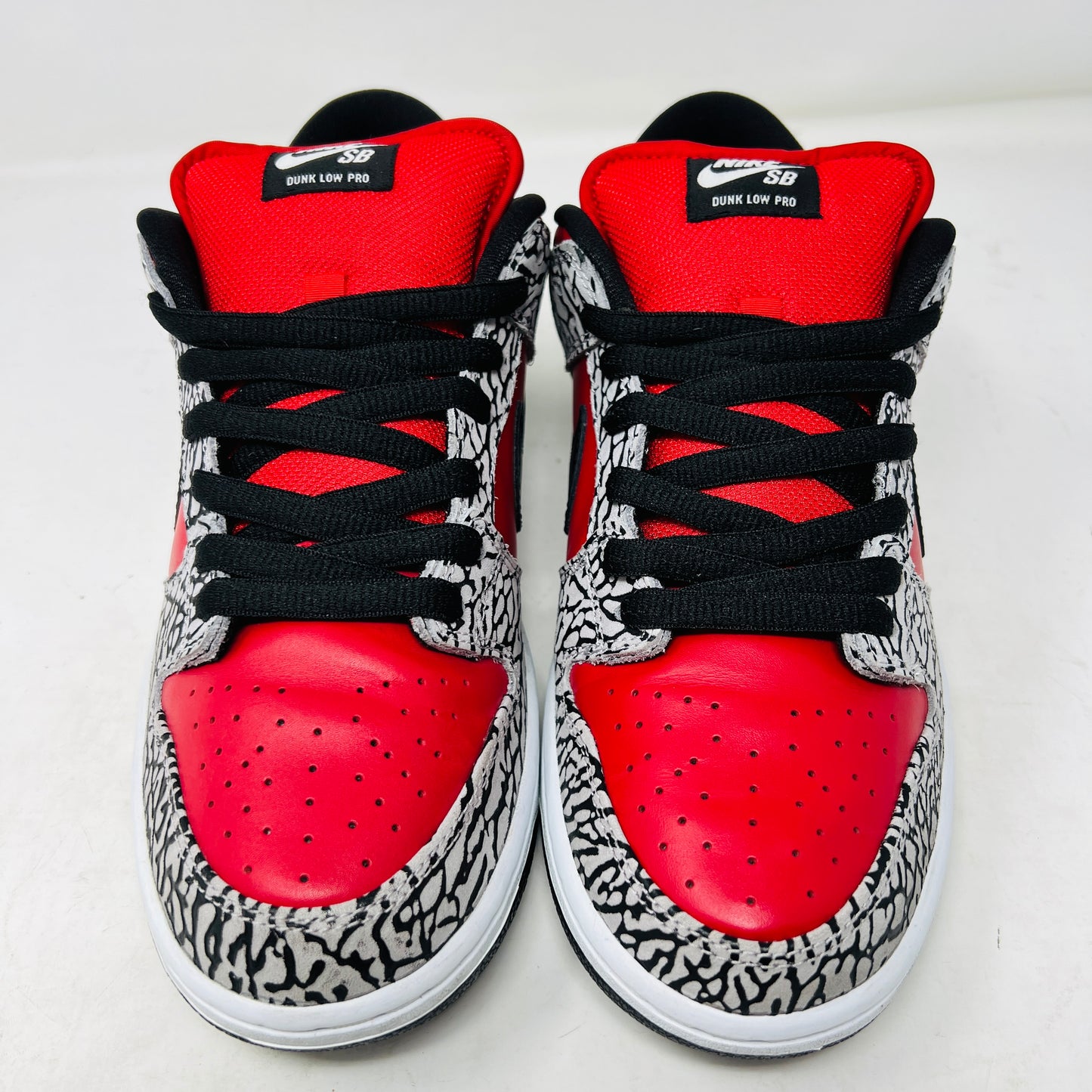 A genuine Nike SB Dunk Low Supreme Red Cement (2012) sneaker, featuring red and black elephant print details, rests on a cardboard box and comes with extra white laces for added style versatility.