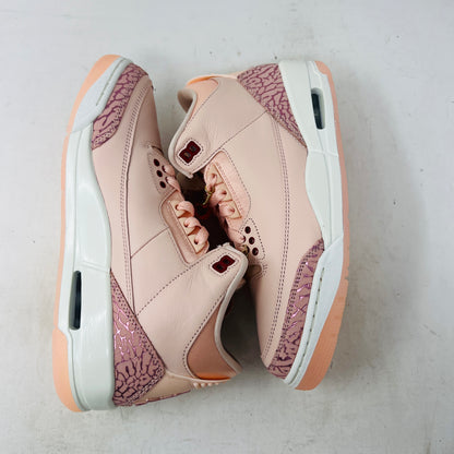 The BRAND NEW Jordan 3 Retro Valentines Day Treat Yourself (2025) (Womens) by Jordan, in pink and cream with textured heel and toe patterns, sits on a closed red shoebox. It features a translucent sole, red eyelets, and an authentic pendant on the laces sparkling like GEMS.