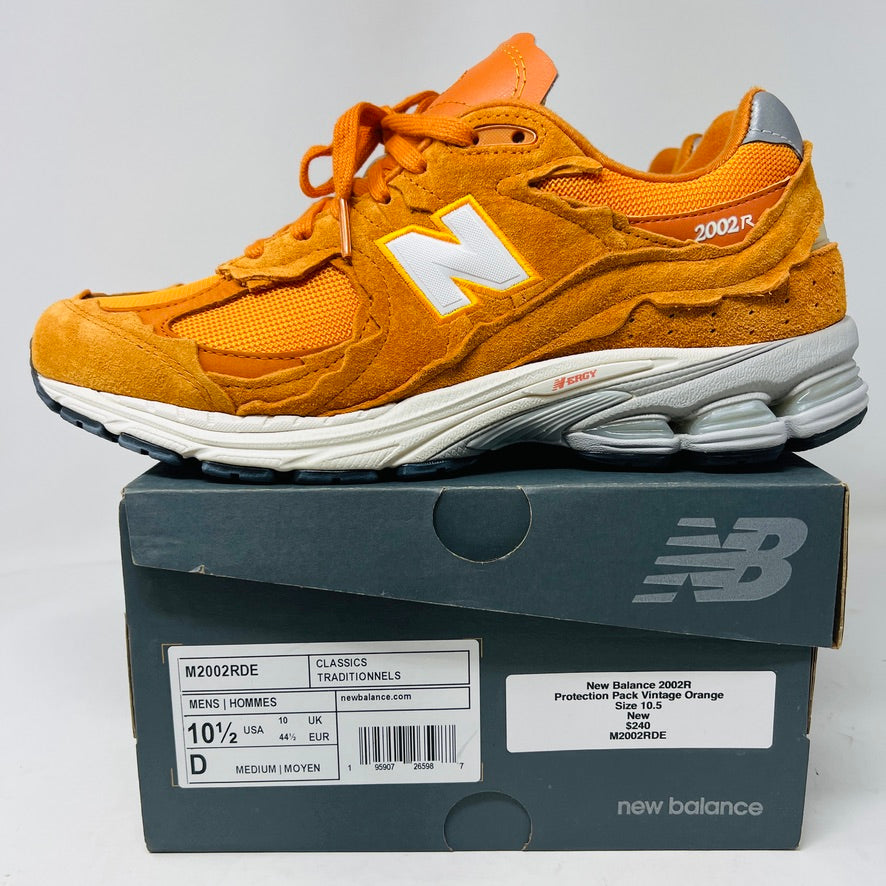 Brand new New Balance 2002R Protection Pack sneakers in Vintage Orange sit on their box, featuring a suede and mesh design, white N logo on sides, gray and white sole. Box in pristine condition with label for mens size 10.5, UK size 9.5.