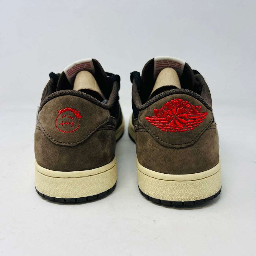 A brown and black Jordan 1 Retro Low OG SP Travis Scott Mocha with clean uppers and a large white swoosh sits on a Nike box. Two sets of extra laces in black and pink beside the box confirm their 100% authenticity. The shoe size is visible on the box label. Released in 2019.