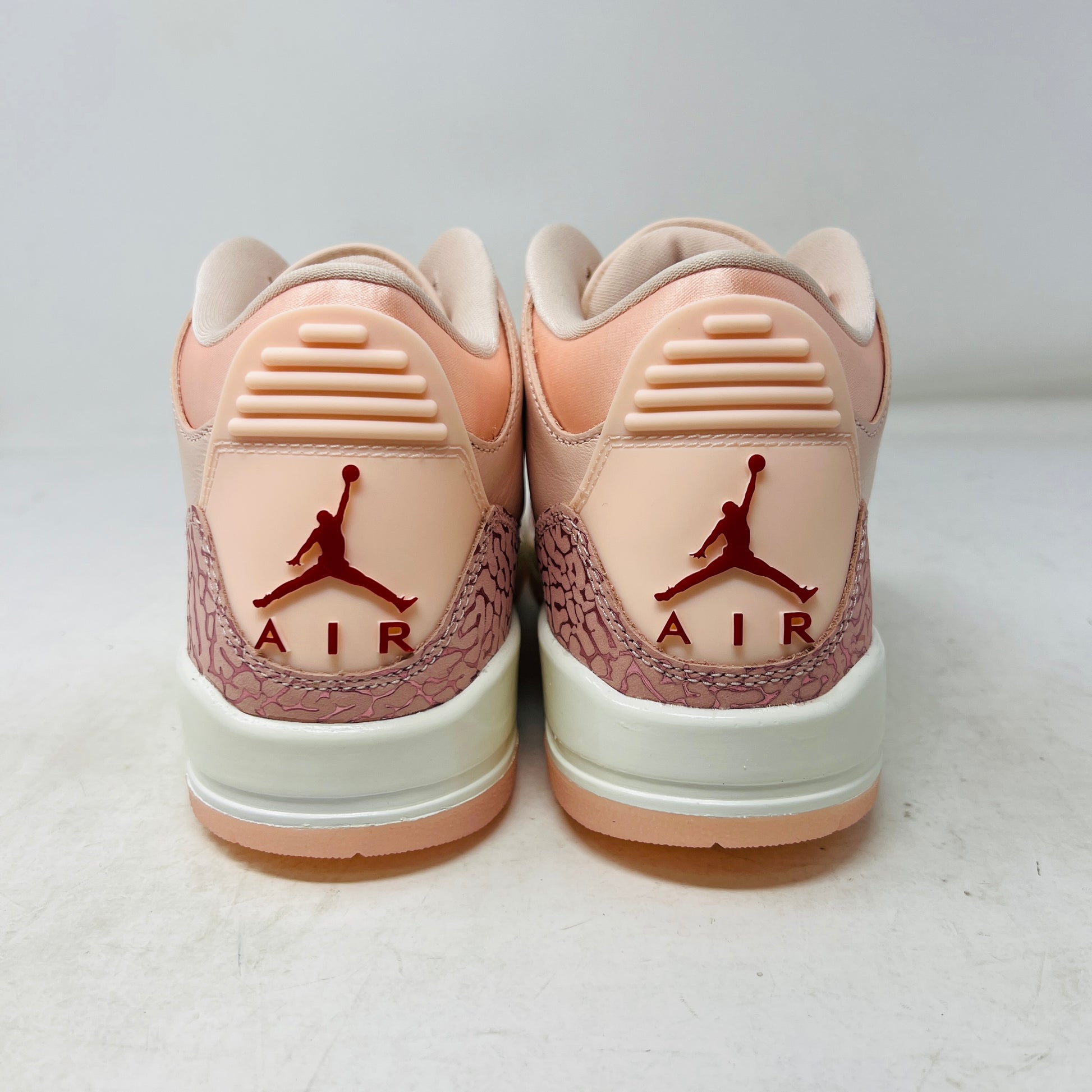 The BRAND NEW Jordan 3 Retro Valentines Day Treat Yourself (2025) (Womens) by Jordan, in pink and cream with textured heel and toe patterns, sits on a closed red shoebox. It features a translucent sole, red eyelets, and an authentic pendant on the laces sparkling like GEMS.