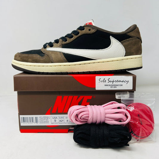 A pair of Jordan 1 Retro Low OG SP Travis Scott Mocha sneakers with a clean upper and white swoosh sits atop a pristine Nike box, with three extra shoelace sets in black, pink, and red neatly arranged beside it.