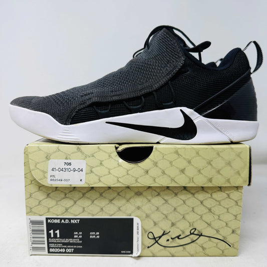 Displayed on a beige box, the Nike Kobe A.D. NXT Black White sneakers feature clean black uppers, a unique lacing system, a white sole, and signature details highlighting their authenticity. The box label indicates US size 11.