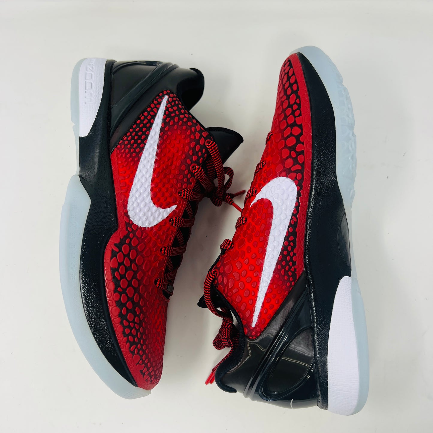 A brand new Kobe Nike Kobe 6 Protro Challenge Red All-Star (2021) sneaker, with a textured pattern and white swoosh, is showcased on a black shoebox. The authentic shoe has a black and white sole, red laces, and ZOOM on the side of the sole.