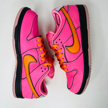 A vibrant pink Nike SB Dunk Low The Powerpuff Girls Blossom sneaker with an orange swoosh sits atop its box. It features clean uppers with black and pink details, orange laces, and comes 100% authentic, including an extra set of black laces beside the box.