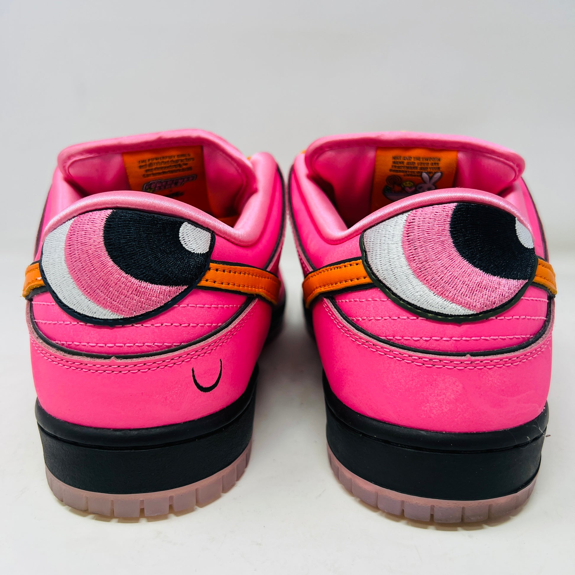 A vibrant pink Nike SB Dunk Low The Powerpuff Girls Blossom sneaker with an orange swoosh sits atop its box. It features clean uppers with black and pink details, orange laces, and comes 100% authentic, including an extra set of black laces beside the box.