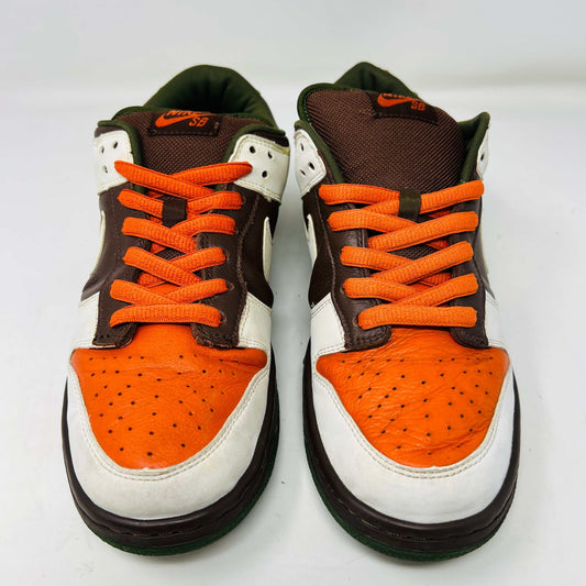 The Nike SB Dunk Low Oompa Loompa sneaker, in a brown, white, and orange color scheme with clean uppers, is displayed on its size 9.5 box. In the foreground is a packet of white laces with a Nike logo—guaranteed 100% authentic.