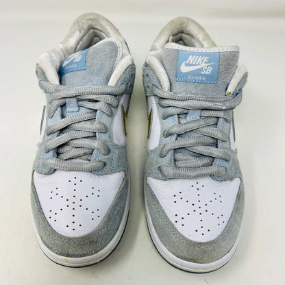 The Nike SB Dunk Low Sean Cliver, a gray and white sneaker with clean uppers and a gold swoosh, is displayed on its yellow-green box. It includes extra white and gold laces for style versatility. The size label reads 7.5, confirming authenticity and the perfect fit.