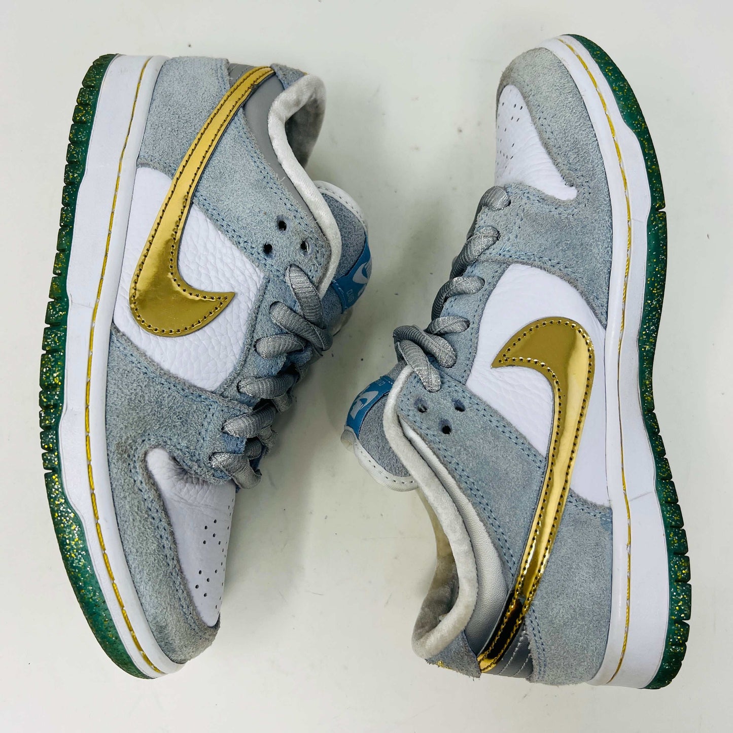 The Nike SB Dunk Low Sean Cliver, a gray and white sneaker with clean uppers and a gold swoosh, is displayed on its yellow-green box. It includes extra white and gold laces for style versatility. The size label reads 7.5, confirming authenticity and the perfect fit.