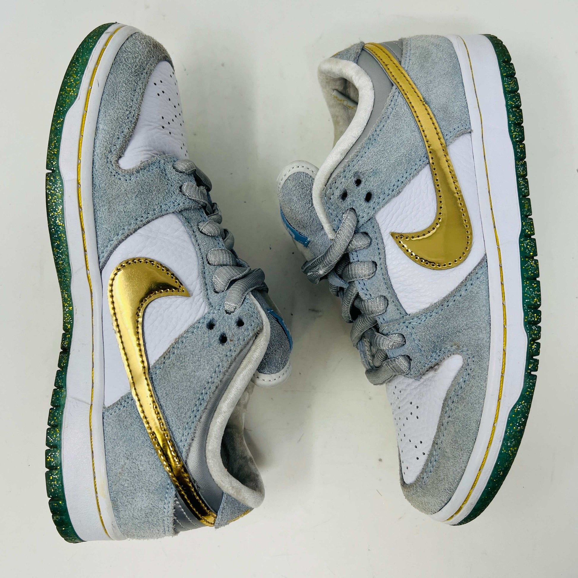 The Nike SB Dunk Low Sean Cliver, a gray and white sneaker with clean uppers and a gold swoosh, is displayed on its yellow-green box. It includes extra white and gold laces for style versatility. The size label reads 7.5, confirming authenticity and the perfect fit.