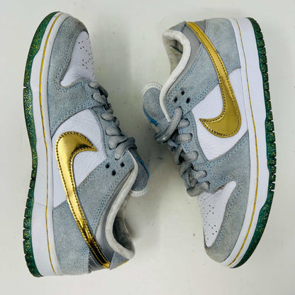 The Nike SB Dunk Low Sean Cliver, a gray and white sneaker with clean uppers and a gold swoosh, is displayed on its yellow-green box. It includes extra white and gold laces for style versatility. The size label reads 7.5, confirming authenticity and the perfect fit.