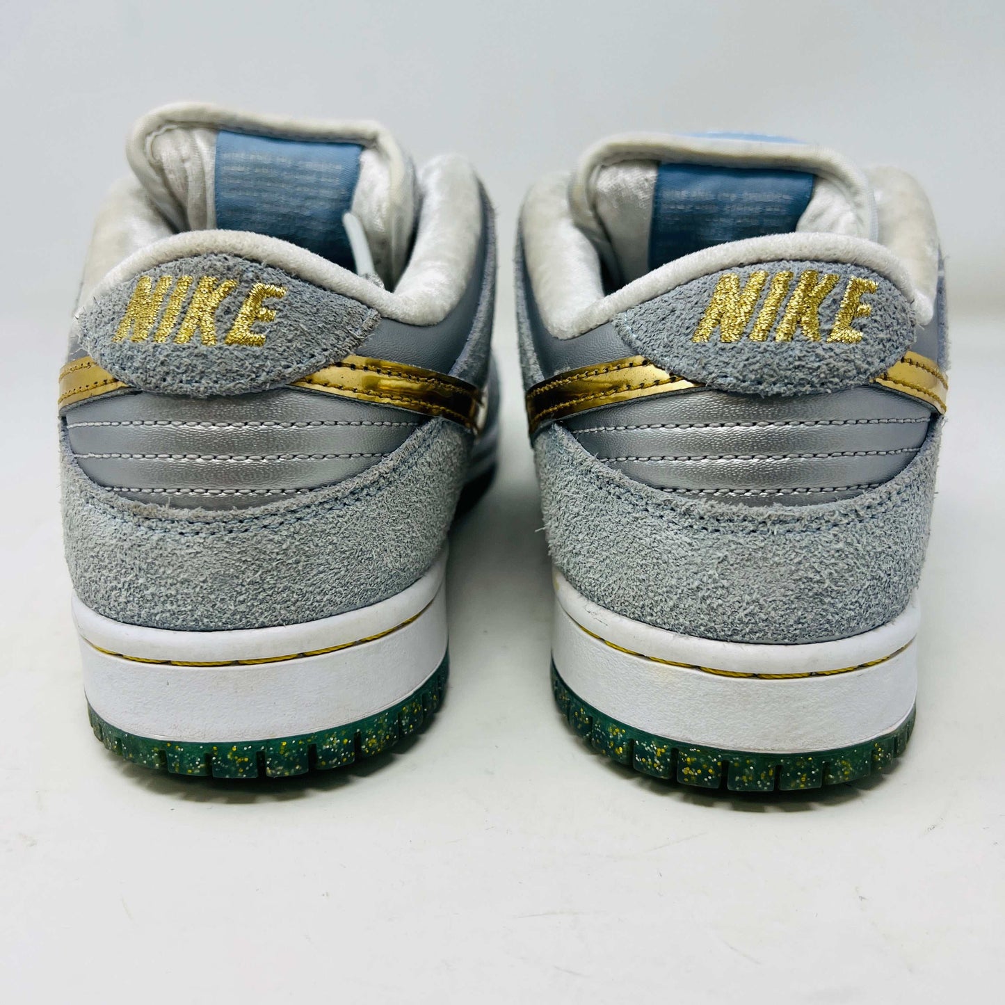 The Nike SB Dunk Low Sean Cliver, a gray and white sneaker with clean uppers and a gold swoosh, is displayed on its yellow-green box. It includes extra white and gold laces for style versatility. The size label reads 7.5, confirming authenticity and the perfect fit.