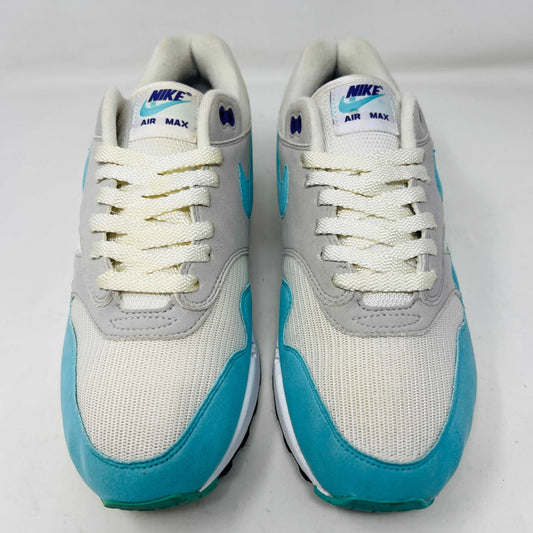 A genuine Nike Air Max 1 Anniversary Aqua sneaker in white, grey, and teal rests on an orange Nike shoebox. It features clean uppers, is size 8.5, and includes a spare laces packet to preserve its classic style.