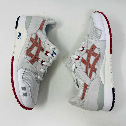 The ASICS Gel-Lyte III Ronnie Fieg Tokyo Trio Yoshino Rose sneaker, featuring clean white and beige uppers with red accents and pink iconic stripes, sits on its box. It includes navy, pink, and beige extra laces, with the authentic size clearly displayed on the box.