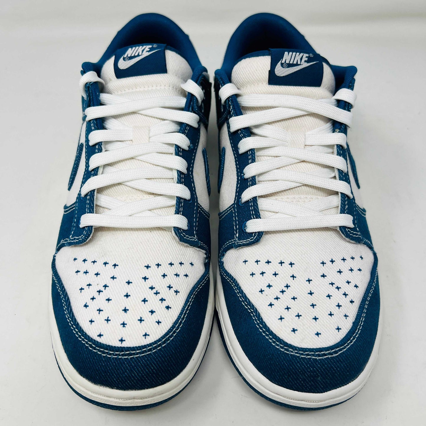 The Nike Dunk Low Industrial Blue Sashiko sneaker, priced at $120, features a white swoosh and lace-up design on a denim-like blue upper and is displayed atop an orange Nike shoebox, guaranteeing authenticity.