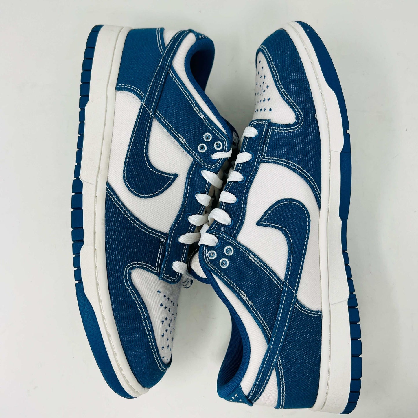 The Nike Dunk Low Industrial Blue Sashiko sneaker, priced at $120, features a white swoosh and lace-up design on a denim-like blue upper and is displayed atop an orange Nike shoebox, guaranteeing authenticity.