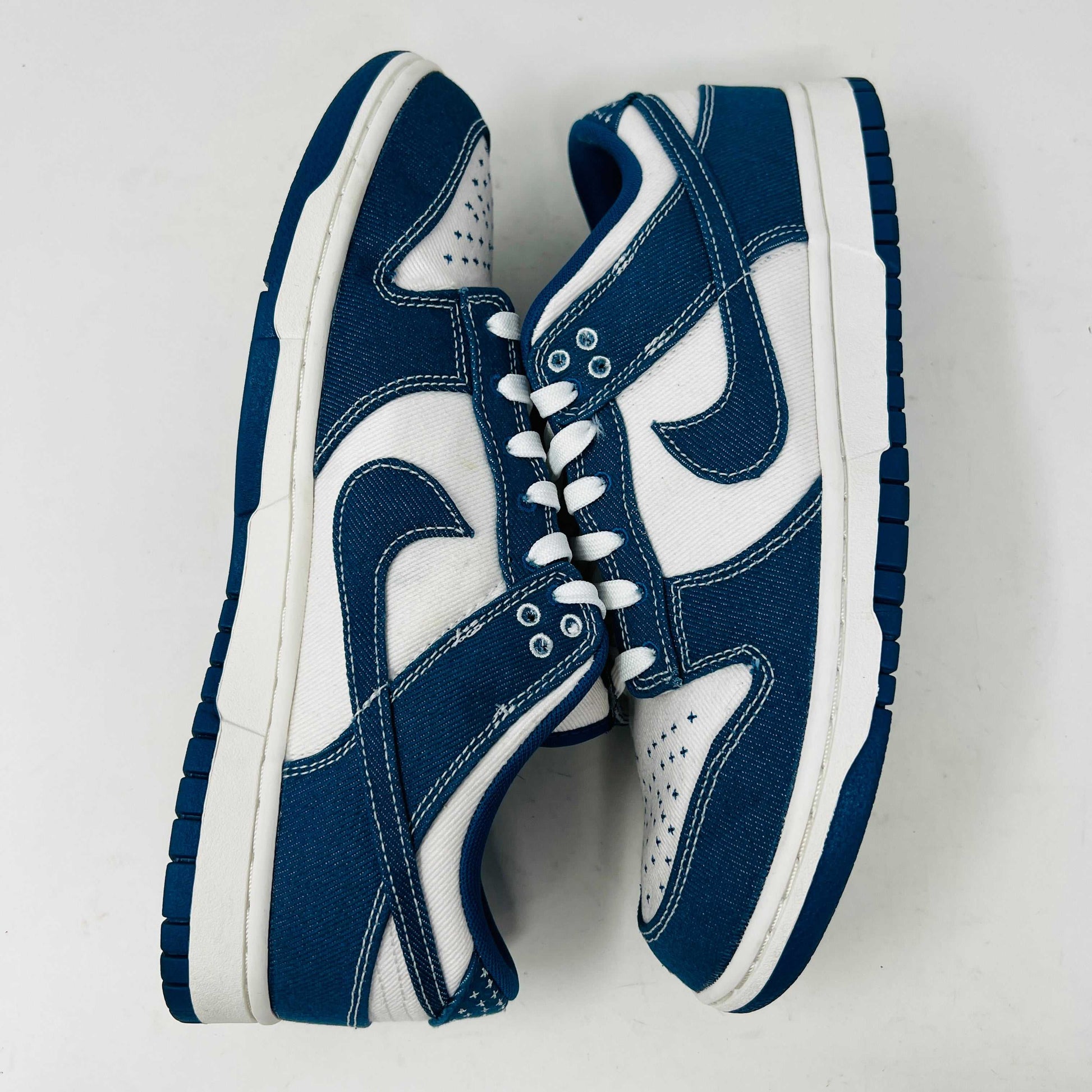 The Nike Dunk Low Industrial Blue Sashiko sneaker, priced at $120, features a white swoosh and lace-up design on a denim-like blue upper and is displayed atop an orange Nike shoebox, guaranteeing authenticity.