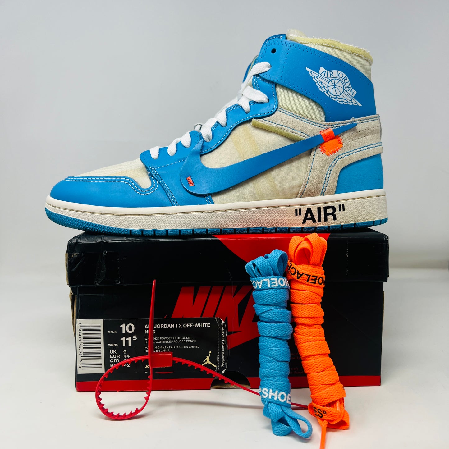 The Jordan 1 Retro High Off-White University Blue sneaker, by Jordan, in blue and white is displayed on a box with AIR text. It includes three extra laces (blue, white, orange), and a red authenticity tag against a pristine white background.