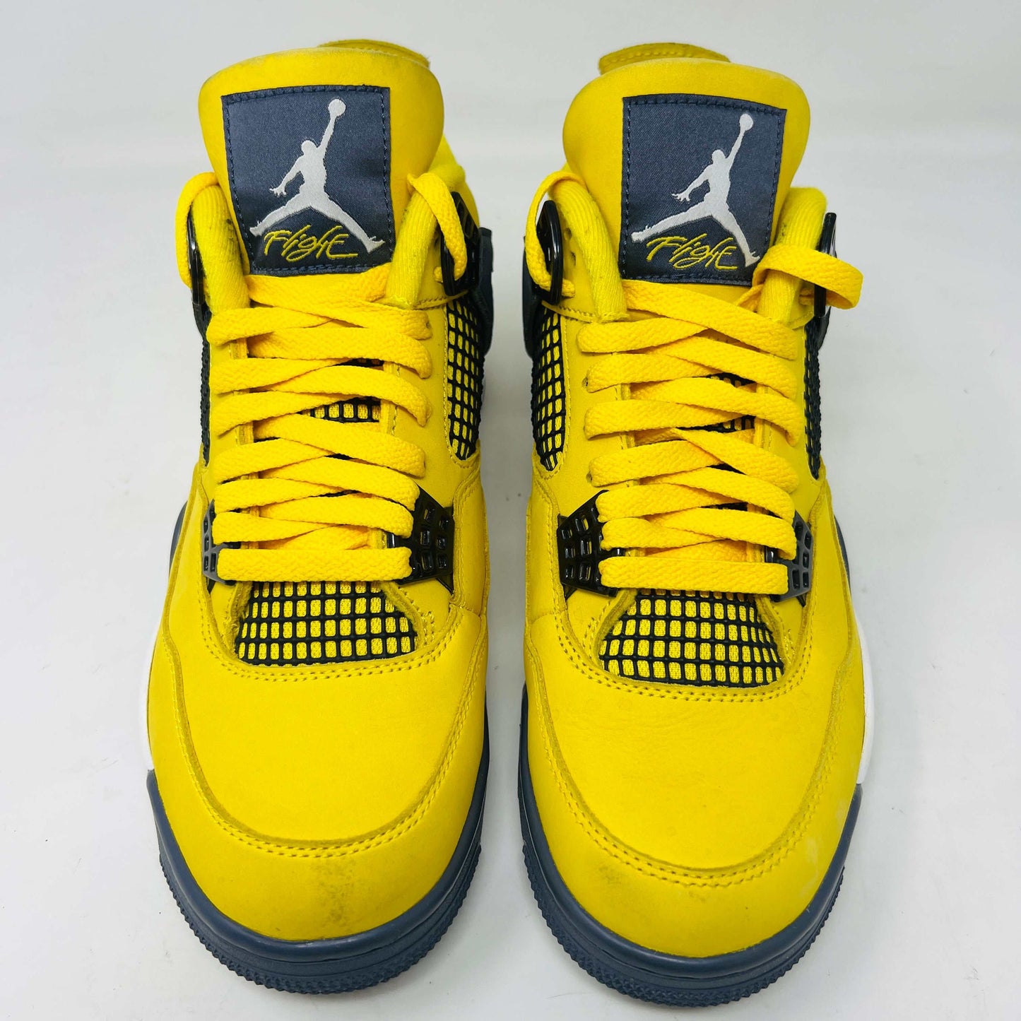 The Jordan 4 Retro Lightning (2021) sneaker, with yellow uppers, black accents, white sole, and gray eyelets, sits on a matching speckled box featuring a black Jumpman logo. Light wear aside, the shoe retains clean uppers for a fresh look.