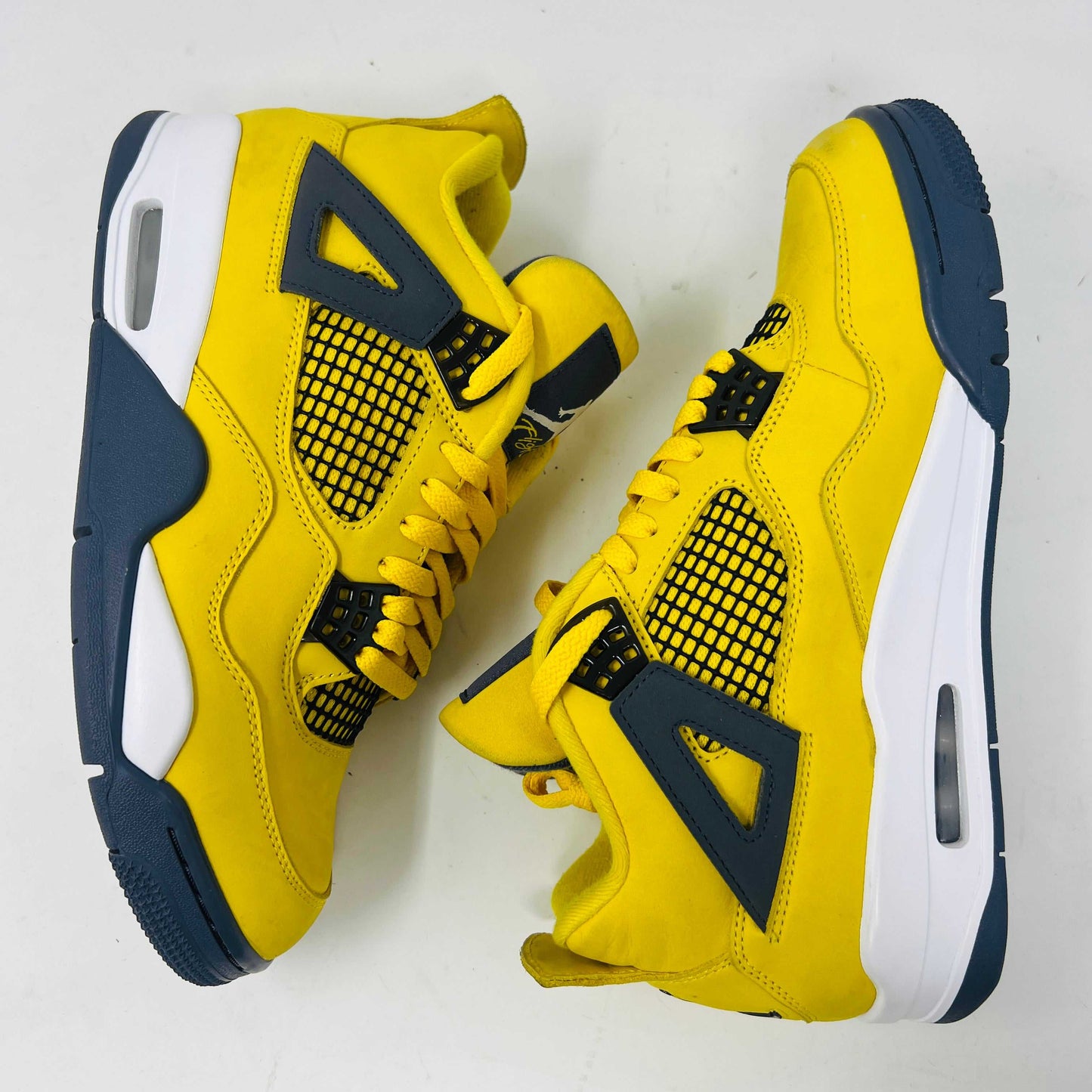 The Jordan 4 Retro Lightning (2021) sneaker, with yellow uppers, black accents, white sole, and gray eyelets, sits on a matching speckled box featuring a black Jumpman logo. Light wear aside, the shoe retains clean uppers for a fresh look.