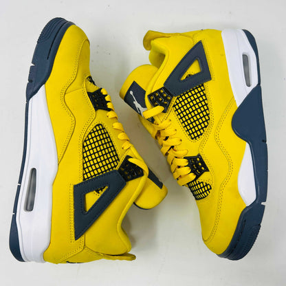 The Jordan 4 Retro Lightning (2021) sneaker, with yellow uppers, black accents, white sole, and gray eyelets, sits on a matching speckled box featuring a black Jumpman logo. Light wear aside, the shoe retains clean uppers for a fresh look.