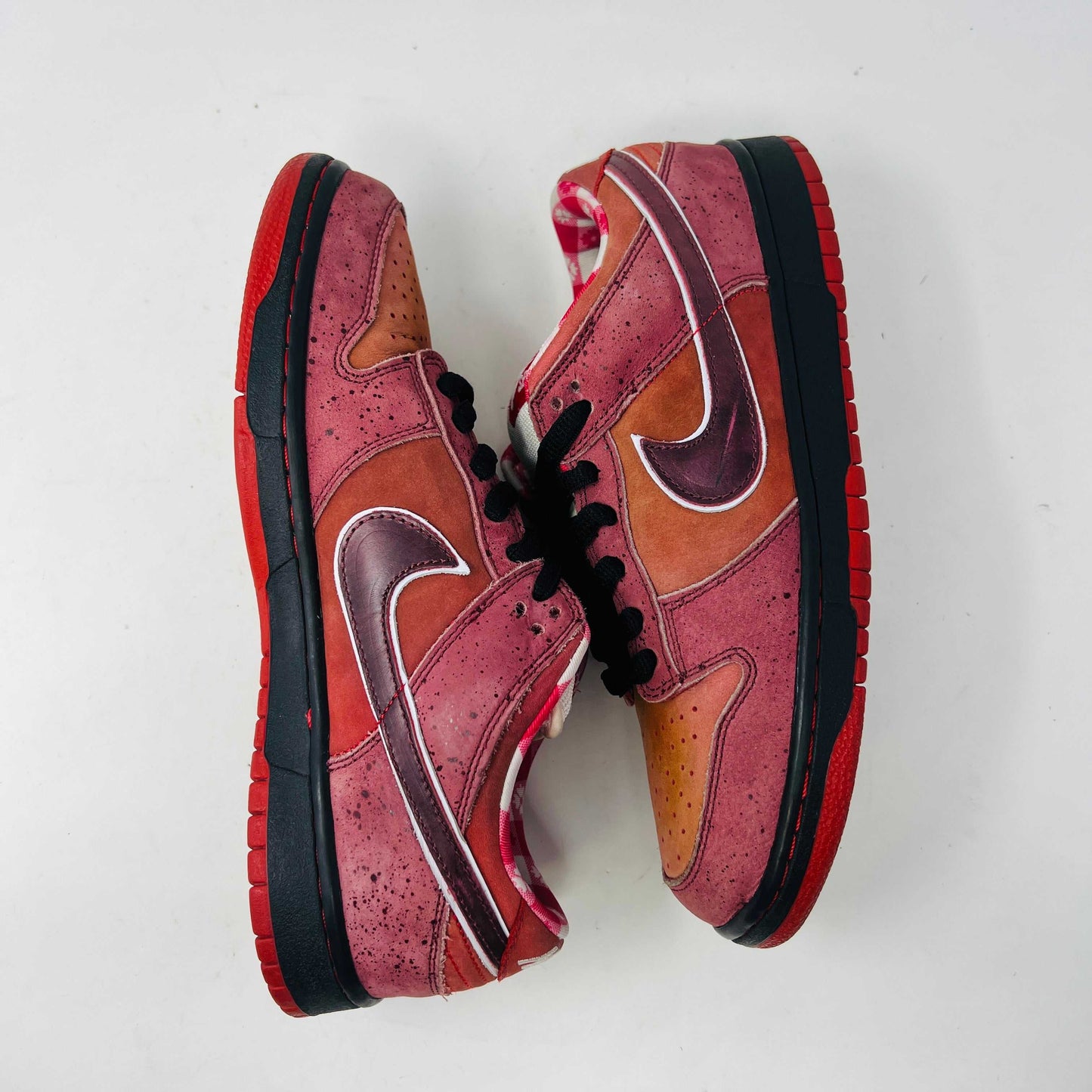 The Nike SB Dunk Low Concepts Red Lobster sneakers feature a stylish gradient from red to orange hues with black laces and a white tongue. They boast a low-cut design, clean uppers, and perforated toes against a white background.