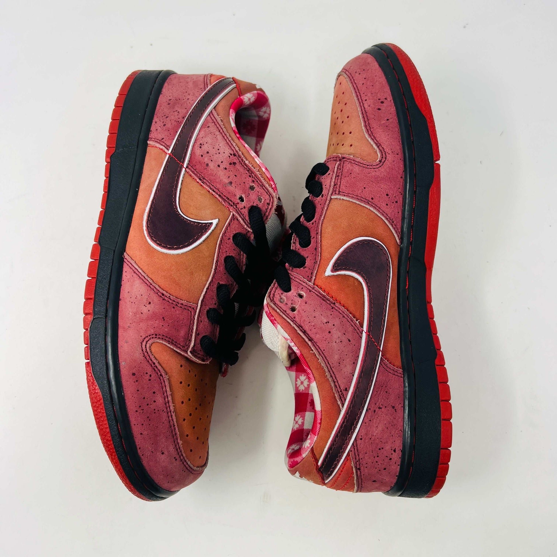 The Nike SB Dunk Low Concepts Red Lobster sneakers feature a stylish gradient from red to orange hues with black laces and a white tongue. They boast a low-cut design, clean uppers, and perforated toes against a white background.