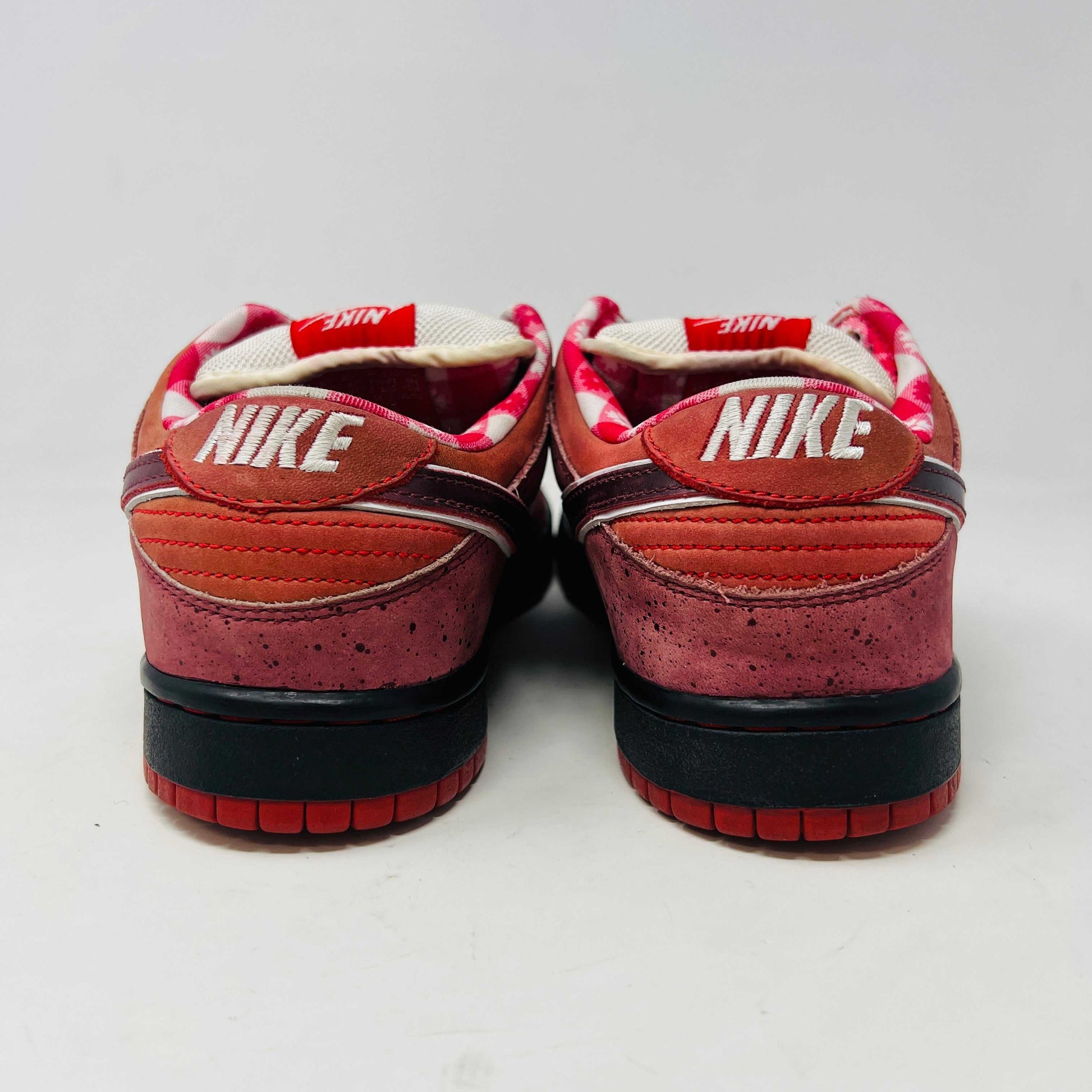 The Nike SB Dunk Low Concepts Red Lobster sneakers feature a stylish gradient from red to orange hues with black laces and a white tongue. They boast a low-cut design, clean uppers, and perforated toes against a white background.