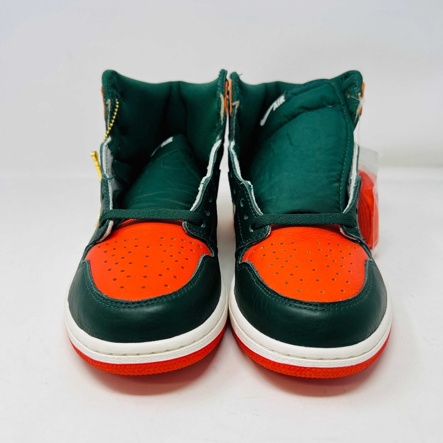 The Jordan 1 Retro High SoleFly Art Basel Sail by Jordan features orange, black, and white leather panels on a red Nike box. A small bag with bright orange laces complements the authentic sneaker, all against a plain white backdrop.