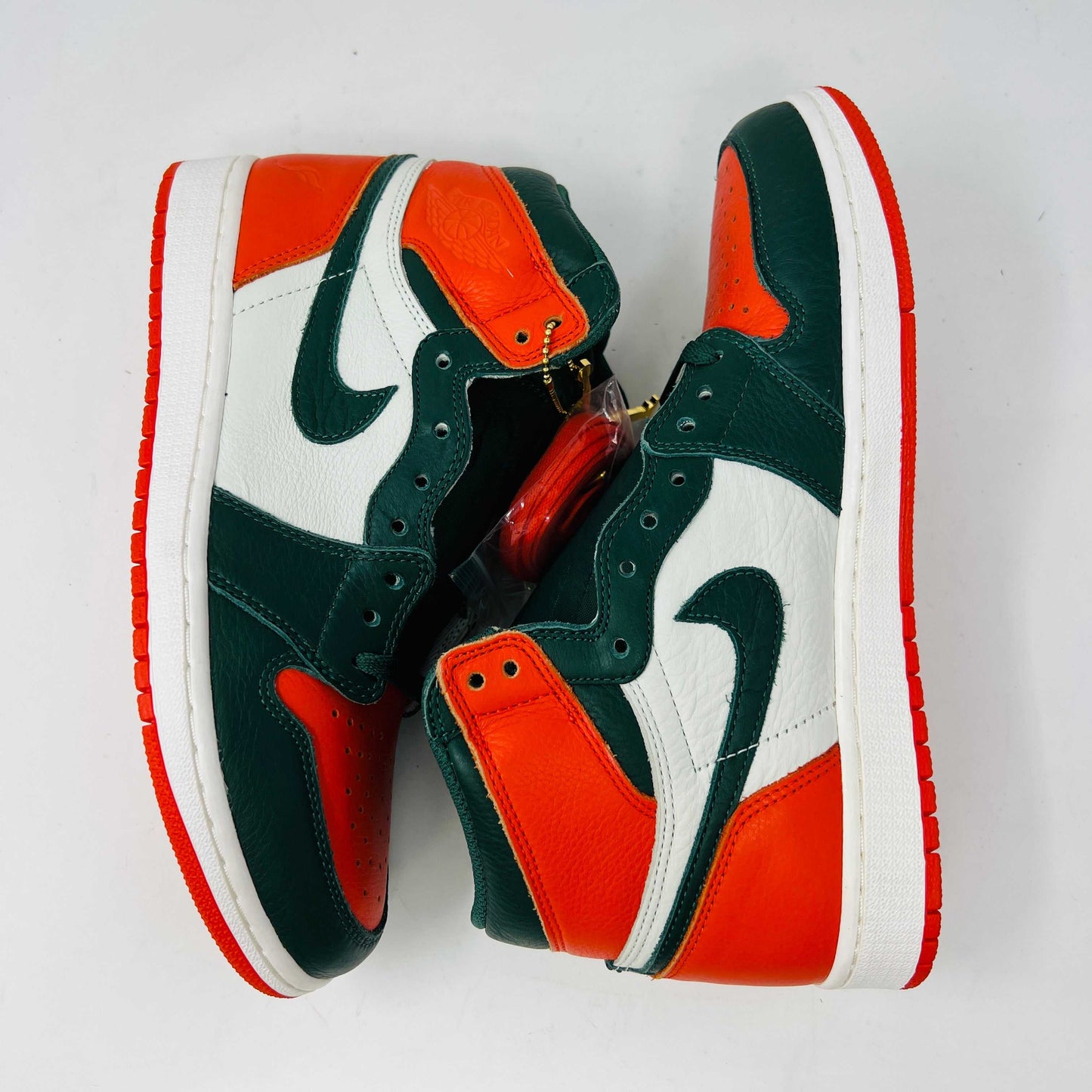 The Jordan 1 Retro High SoleFly Art Basel Sail by Jordan features orange, black, and white leather panels on a red Nike box. A small bag with bright orange laces complements the authentic sneaker, all against a plain white backdrop.