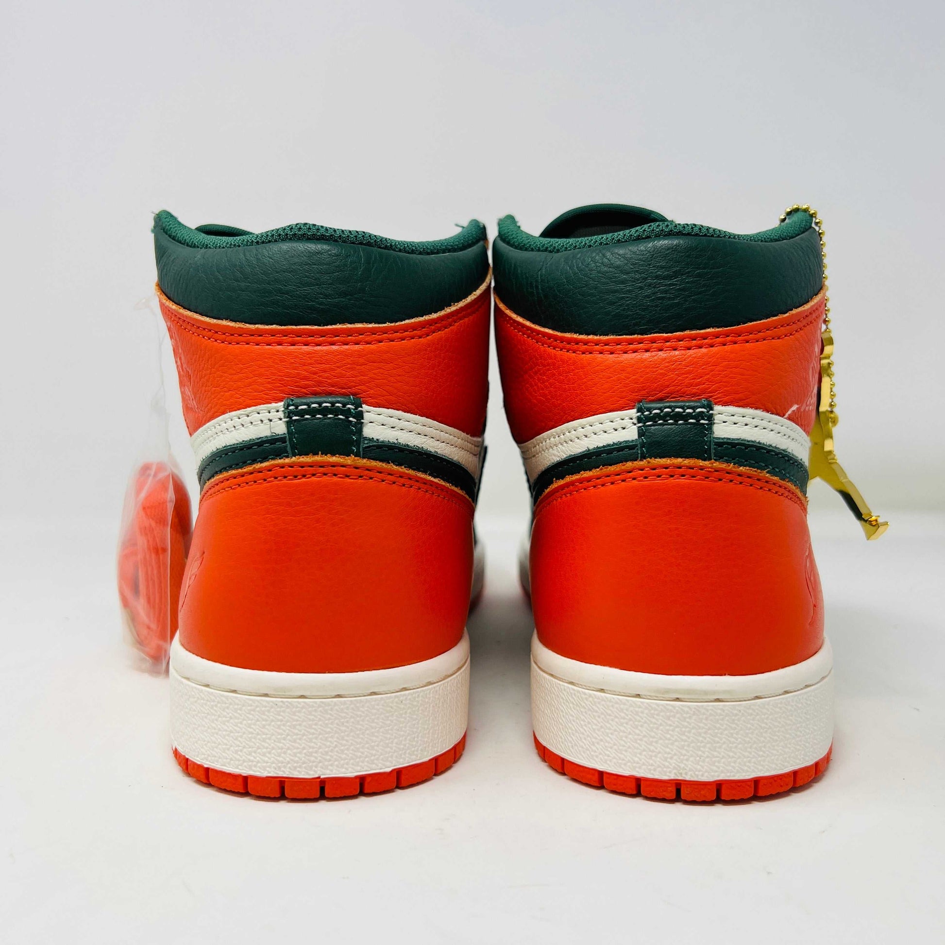 The Jordan 1 Retro High SoleFly Art Basel Sail by Jordan features orange, black, and white leather panels on a red Nike box. A small bag with bright orange laces complements the authentic sneaker, all against a plain white backdrop.