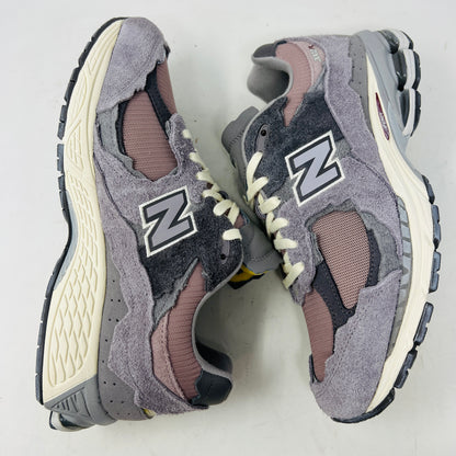 A pair of New Balance 2002R Protection Pack Lunar New Year Dusty Lilac sneakers mix gray and beige tones with CLEAN UPPERS and a textured design. Displayed on a shoebox, they include extra maroon laces. The box label details the shoe size and model.