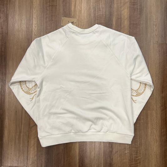 The Nike Kobe Tech Fleece Crew by KOBE is a new white sweatshirt with a small dark chest emblem and gold snake patterns on both sleeves, displayed on a wooden floor with its price tag near the neckline.