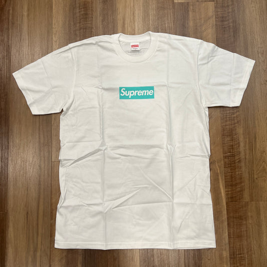 The Supreme Tiffany & Co. Box Logo Tee White, featuring a mint green logo with crisp Supreme text, is laid flat on a wooden floor in pristine condition with slight creases.