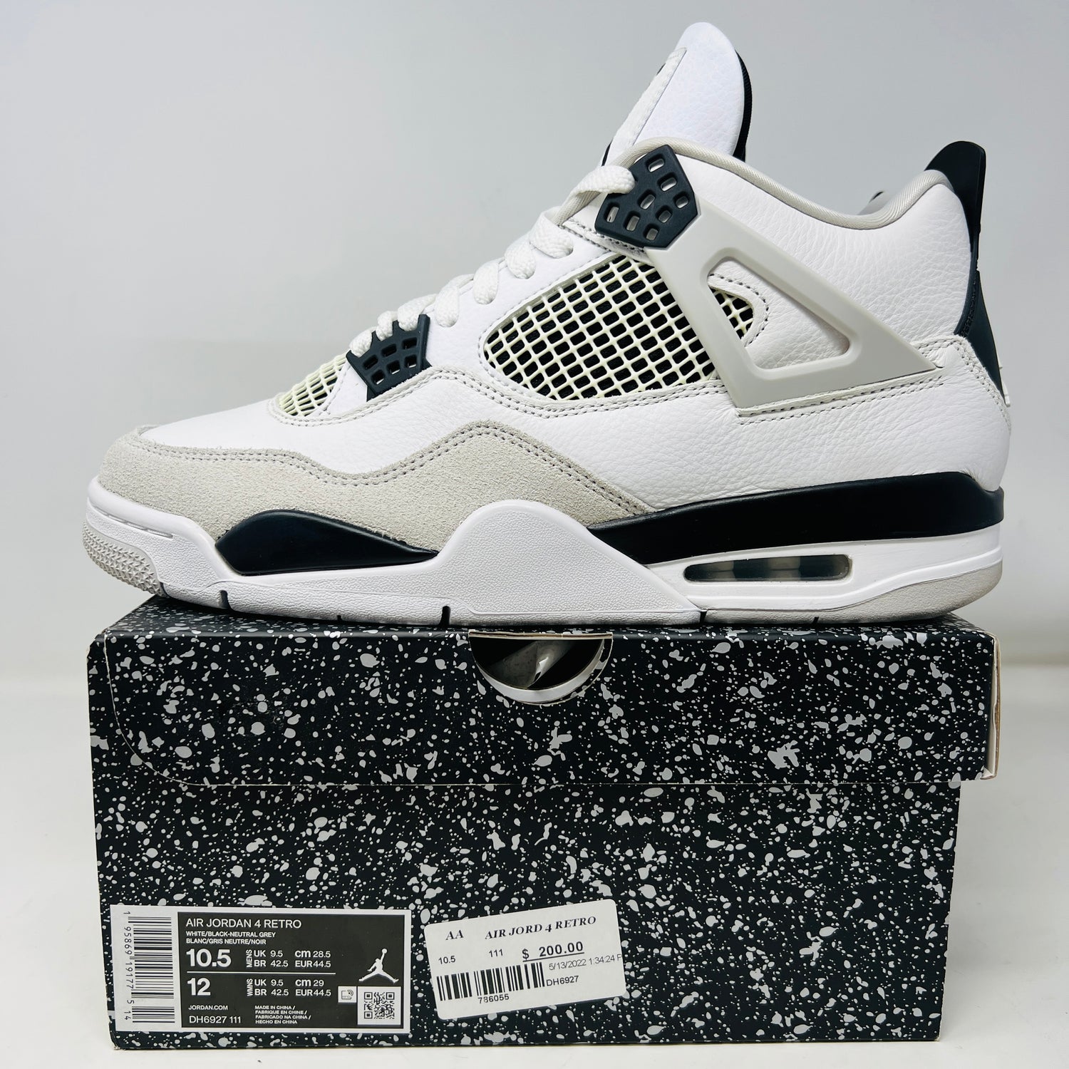 The Jordan 4 Retro Military Black, a 2022 release in white and black with clean uppers, is showcased on its speckled black shoebox. The size 10.5 sneaker is priced at $200 and includes mesh netting and plastic detailing, enhancing durability to prevent heel drag.