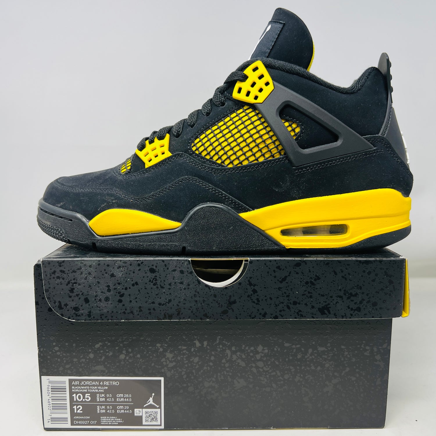 The Jordan 4 Retro Thunder (2023) sneaker in black and vibrant yellow mesh is displayed on its speckled box, which remains in pristine condition with visible sizing info.