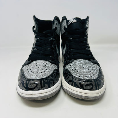 A gray and black Jordan 1 Retro High OG Rebellionaire sneaker with a graffiti-style design sits on a black Nike shoebox featuring the Nike logo and size details. Slight heel drag indicates its journey.