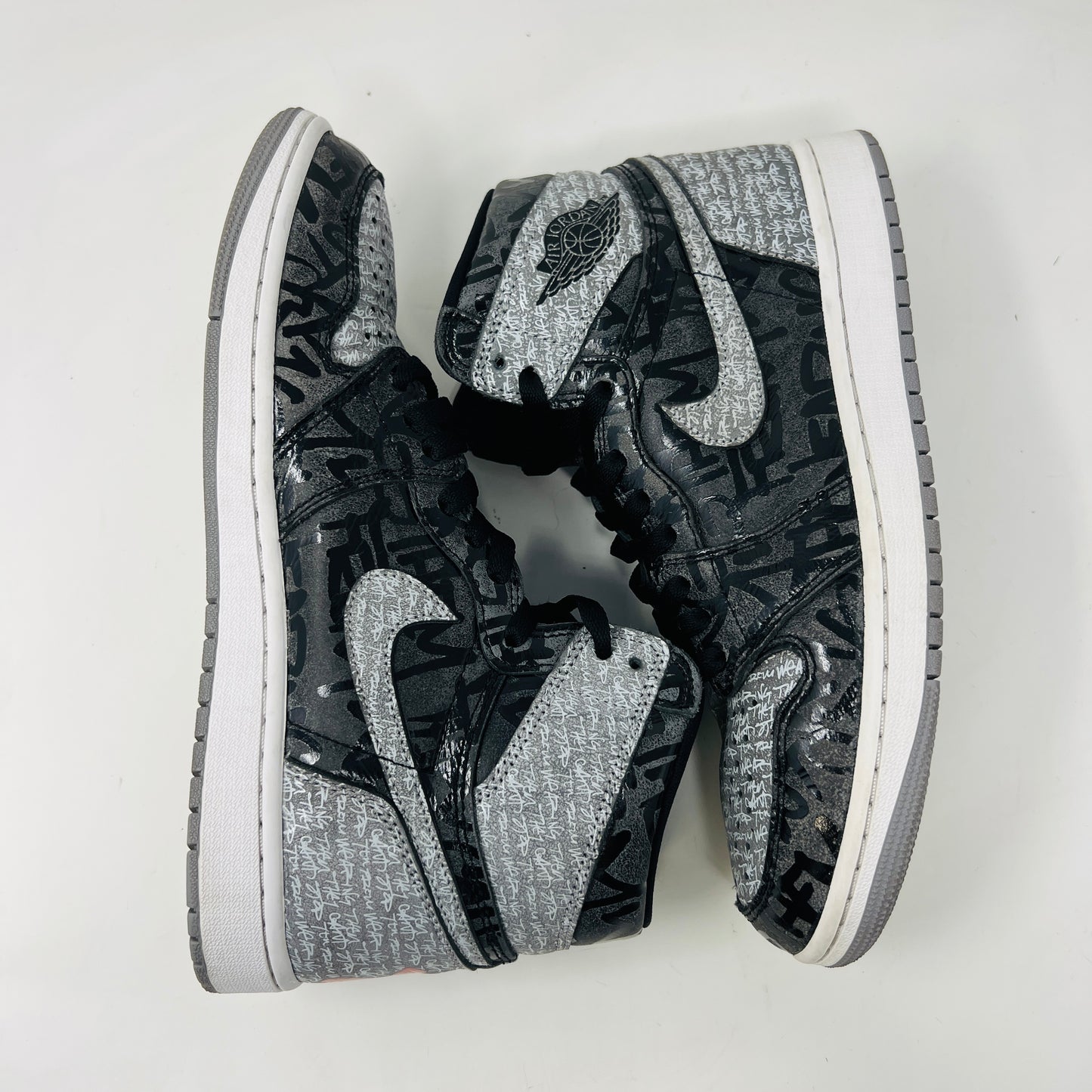 A gray and black Jordan 1 Retro High OG Rebellionaire sneaker with a graffiti-style design sits on a black Nike shoebox featuring the Nike logo and size details. Slight heel drag indicates its journey.