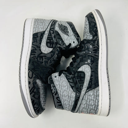 A gray and black Jordan 1 Retro High OG Rebellionaire sneaker with a graffiti-style design sits on a black Nike shoebox featuring the Nike logo and size details. Slight heel drag indicates its journey.