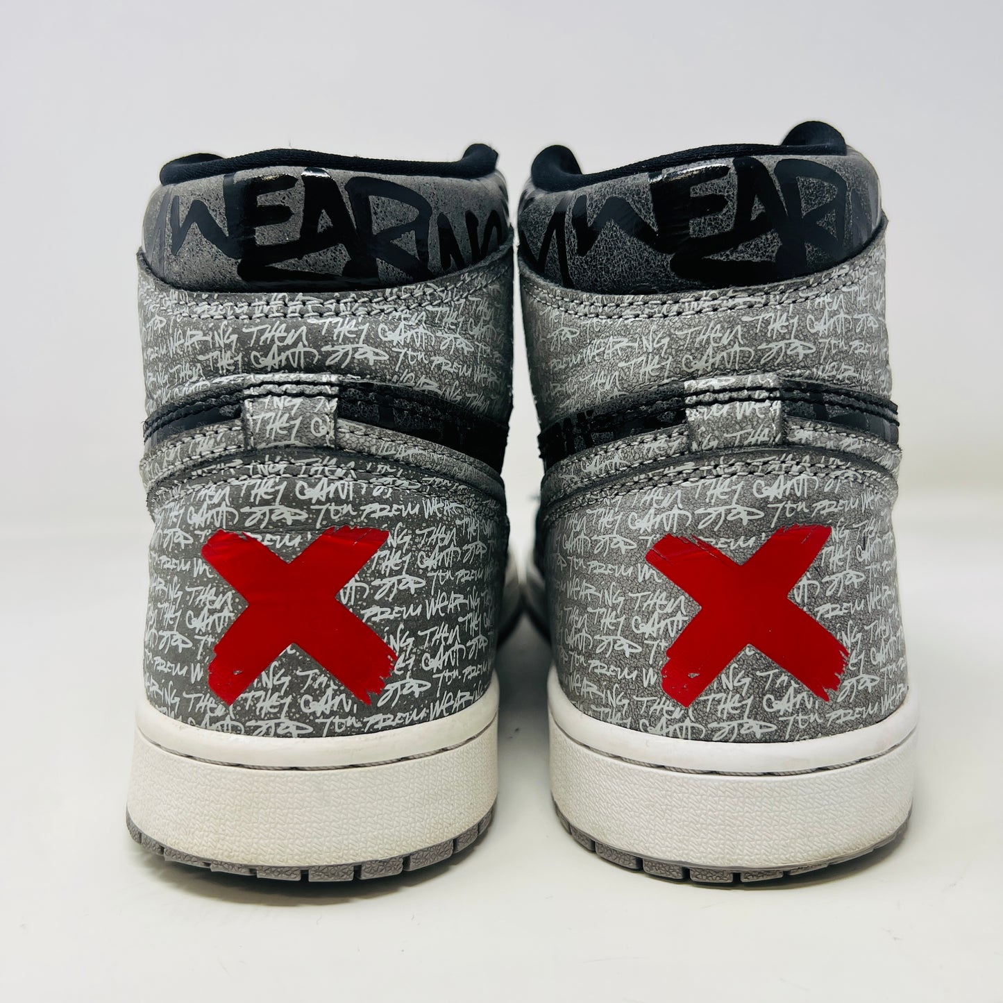 A gray and black Jordan 1 Retro High OG Rebellionaire sneaker with a graffiti-style design sits on a black Nike shoebox featuring the Nike logo and size details. Slight heel drag indicates its journey.