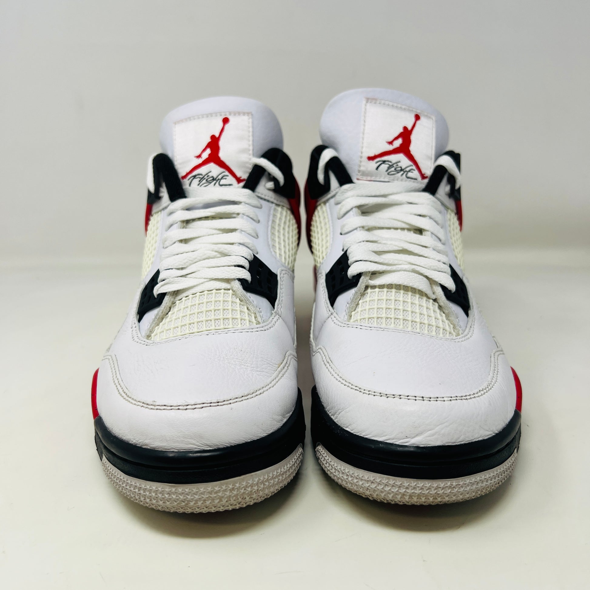 The Jordan 4 Retro Red Cement sneaker, white with red and black accents and featuring visible air cushioning and signature side netting, is displayed on its immaculate black shoebox. The box label indicates a size 9.