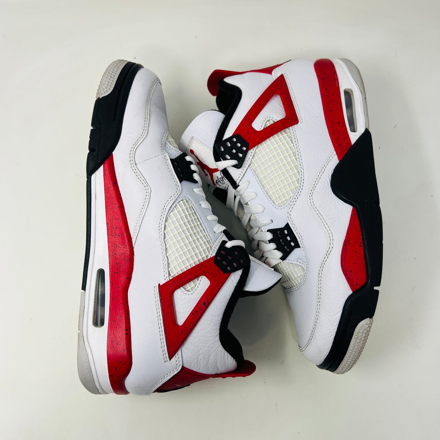 The Jordan 4 Retro Red Cement sneaker, white with red and black accents and featuring visible air cushioning and signature side netting, is displayed on its immaculate black shoebox. The box label indicates a size 9.