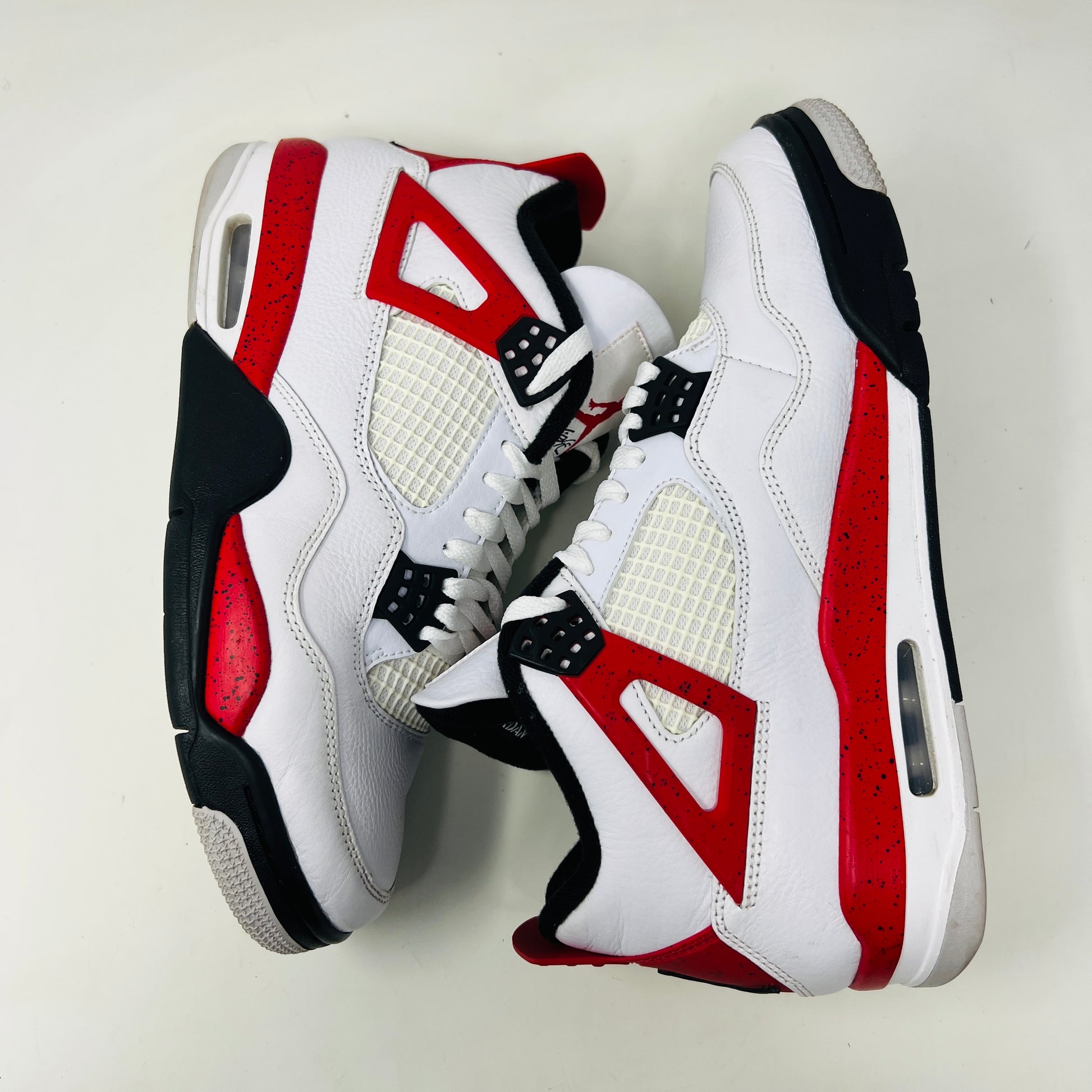 The Jordan 4 Retro Red Cement sneaker, white with red and black accents and featuring visible air cushioning and signature side netting, is displayed on its immaculate black shoebox. The box label indicates a size 9.