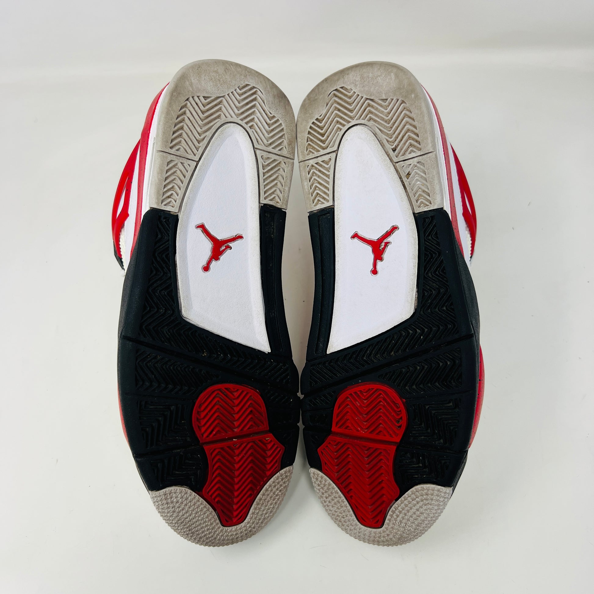 The Jordan 4 Retro Red Cement sneaker, white with red and black accents and featuring visible air cushioning and signature side netting, is displayed on its immaculate black shoebox. The box label indicates a size 9.