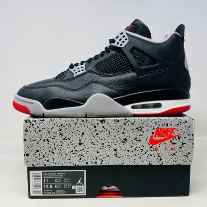 A Jordan 4 Retro Bred Reimagined sneaker in black and red sits on its good condition box, showcasing textured black leather uppers, red accents, and a white midsole. The box has a speckled design featuring the iconic Nike Air logo.